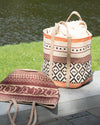 Woven bags with geometric patterns on a wooden surface by a body of water.