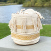 Decorative woven basket with tassels on a wooden surface near a body of water.
