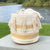 Decorative woven basket with tassels on a wooden surface near a body of water.