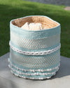 Woven basket with blue, white, and beige stripes on a wooden surface with grass in the background