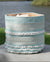 Woven basket with blue and white pattern on a wooden surface near a body of water.
