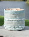 Decorative woven basket with blue and white pattern on a wooden surface near a body of water.