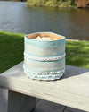 Woven basket with blue and white stripes on a wooden surface by a lake