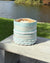 Woven basket with blue and white stripes on a wooden surface by a lake