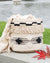 Woven bag with black accents and fringes on a wooden surface near a body of water.