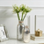 Two silver glittery vases with flowers on a white surface with a neutral background