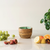 Wooden bowl with a green interior on a light surface with fruits and a plant.