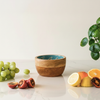 Wooden bowl with a blue interior on a light surface with fruits and a plant.