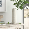 White textured vase on a wooden surface with a plant and books in the background