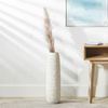 White textured vase with dried pampas grass against a light wall with a wooden side table.
