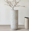 Decorative vase with geometric pattern on a light wooden floor against a white wall.