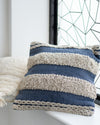 Textured blue and beige pillow on a white surface with a geometric window in the background