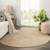 Round woven rug in a living room with a couch, lamp, and plants.