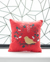 Red pillow with a bird design on a white surface with a geometric patterned wall in the background