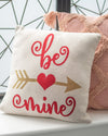 Decorative pillow with 'be mine' text and heart design on a neutral background