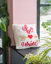 Decorative pillow with 'be mine' text on a shelf with plants around