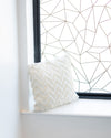 White pillow on a windowsill with geometric wall art in the background