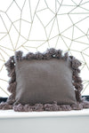 Gray pillow with pom-pom trim against a geometric wall pattern