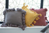 Three decorative pillows with tassels on a windowsill with a geometric window design in the background.