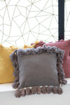 Gray pillow with tassels on a white surface with a geometric wall pattern in the background