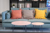 Blue sofa with colorful pillows and two round tables in a living room setting.
