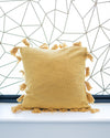 Yellow pillow with tassels on a white surface against a geometric patterned wall.