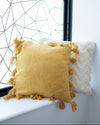Yellow pillow with tassels on a windowsill with a geometric wall design in the background.
