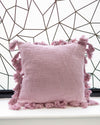 Pink pillow with tassels on a white surface against a geometric black and white wall.