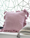Pink pillow with tassels on a surface with a geometric wall pattern in the background