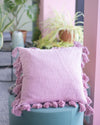 Pink pillow with tassels on a teal stool in a blurred indoor setting