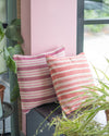 Striped cushions on a chair with a pink wall and plants in the background