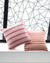 Two striped cushions on a white surface with a geometric patterned wall in the background.